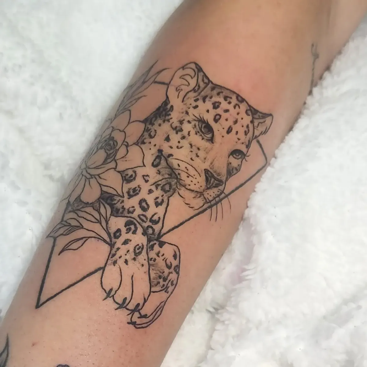 Tatuagem de onça em fine line com composição floral no antebraço, feita no Ateliê Garden